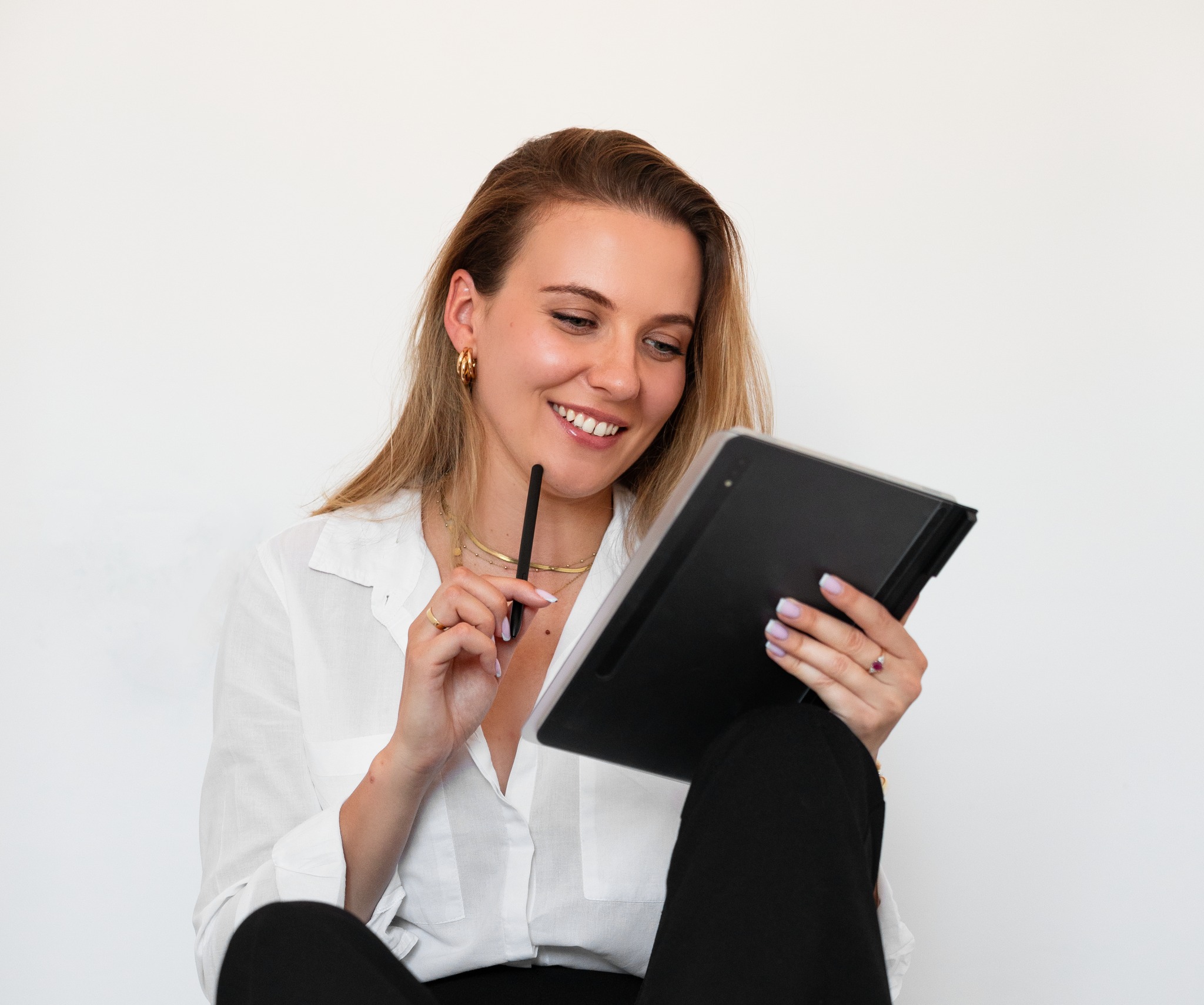 Uśmiechnięta blondynka w białej koszuli, z czarnym tabletem graficznym i rysikiem w dłoni, analizuje projekt.