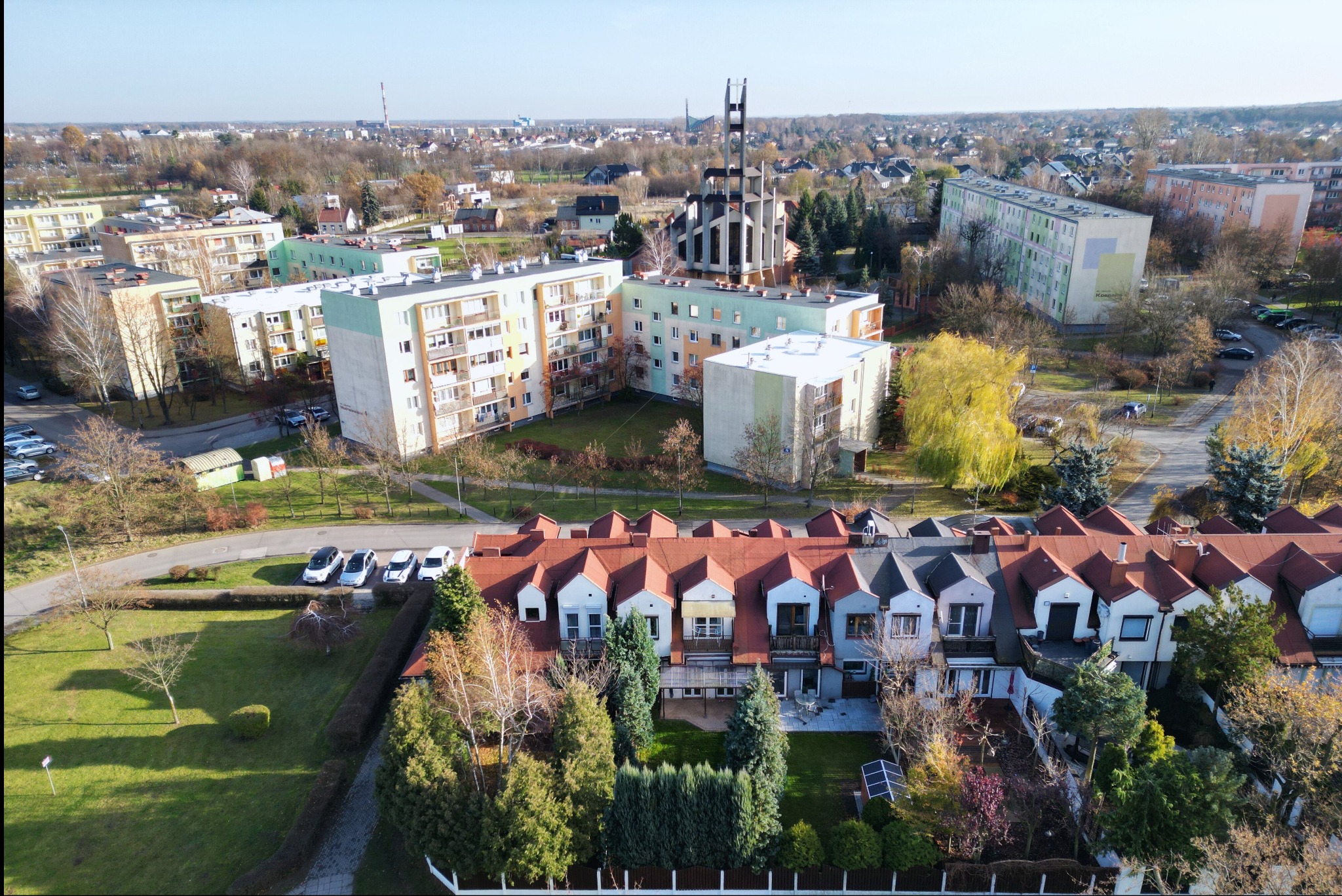 Panorama osiedla mieszkaniowego z blokami i szeregowcami, widok z góry w słoneczny dzień, na horyzoncie wieża kościoła