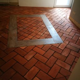 Przedsiębiorstwo Budowlane - Ułożona podłoga z czerwonej cegły w jodełkę, z drewnianą ramą w kształcie kwadratu.