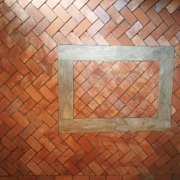 Przedsiębiorstwo Budowlane - Ułożona ceglana podłoga w jodełkę z drewnianą ramą wokół centralnej sekcji ułożonej w kwadraty.