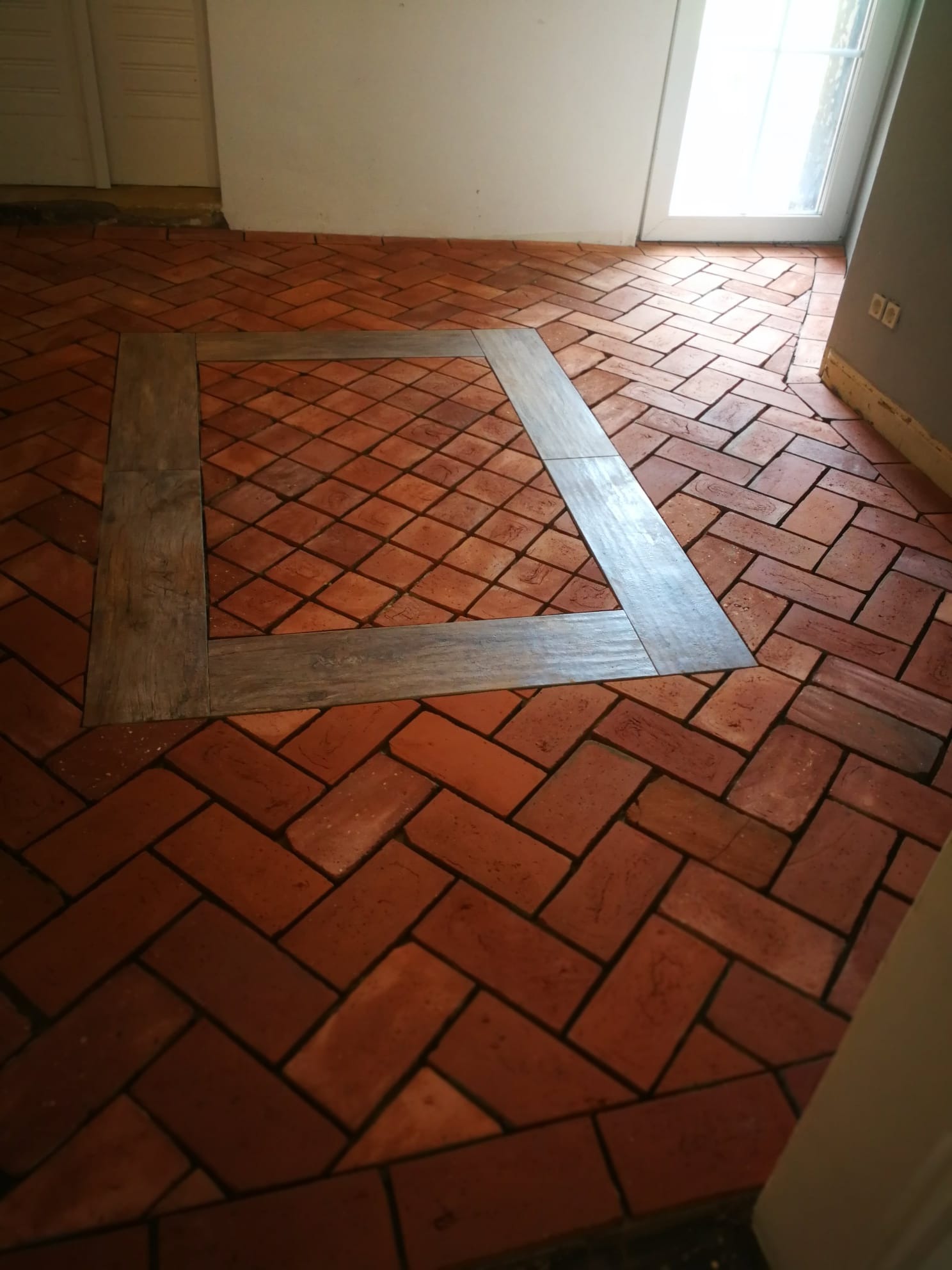 Ułożona podłoga z czerwonej cegły w jodełkę, z drewnianą ramą w kształcie kwadratu.