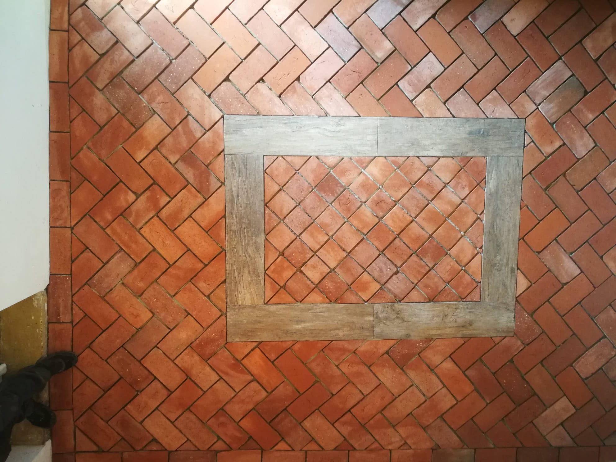 Ułożona ceglana podłoga w jodełkę z drewnianą ramą wokół centralnej sekcji ułożonej w kwadraty.