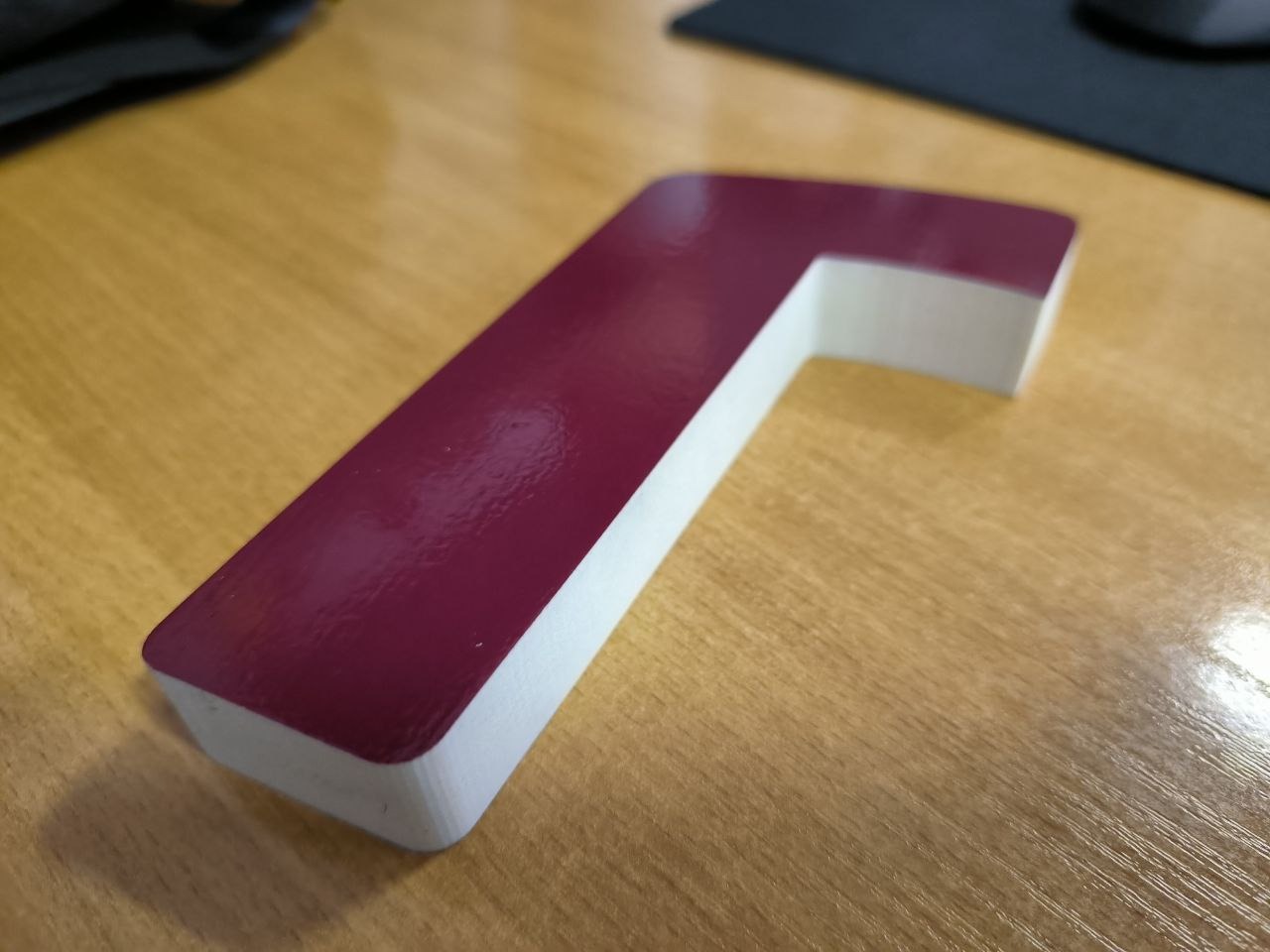 Litera 3D w kolorze burgundowym z białymi bokami, leżąca na drewnianym biurku, sfotografowana z bliska.