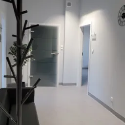 Jasne wnętrze poczekalni z czarnym wieszakiem na ubrania w kształcie drzewa, sofą i zegarem na ścianie