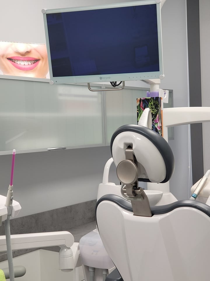 Wnętrze gabinetu dentystycznego: fotel pacjenta, monitor z logo 'oncovo' oraz plakat z uśmiechem w aparacie ortodontycznym.