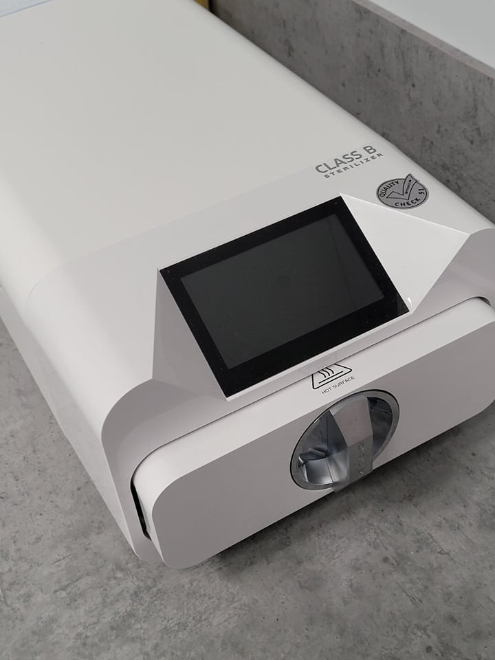 Autoklaw stomatologiczny klasy B z wyświetlaczem, oznaczony symbolem ostrzegawczym 'gorąca powierzchnia', na szarym blacie.