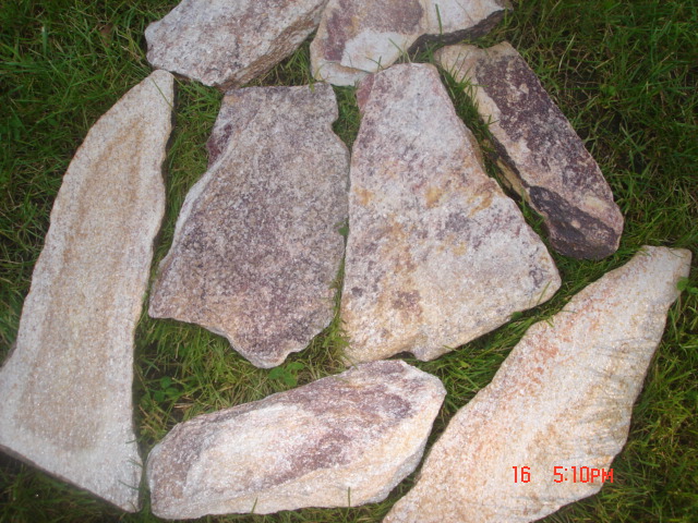 Nieregularne płyty kamienne w odcieniach beżu i brązu, ułożone na trawie w świetle dziennym, z widoczną datą i godziną na dole kadru.