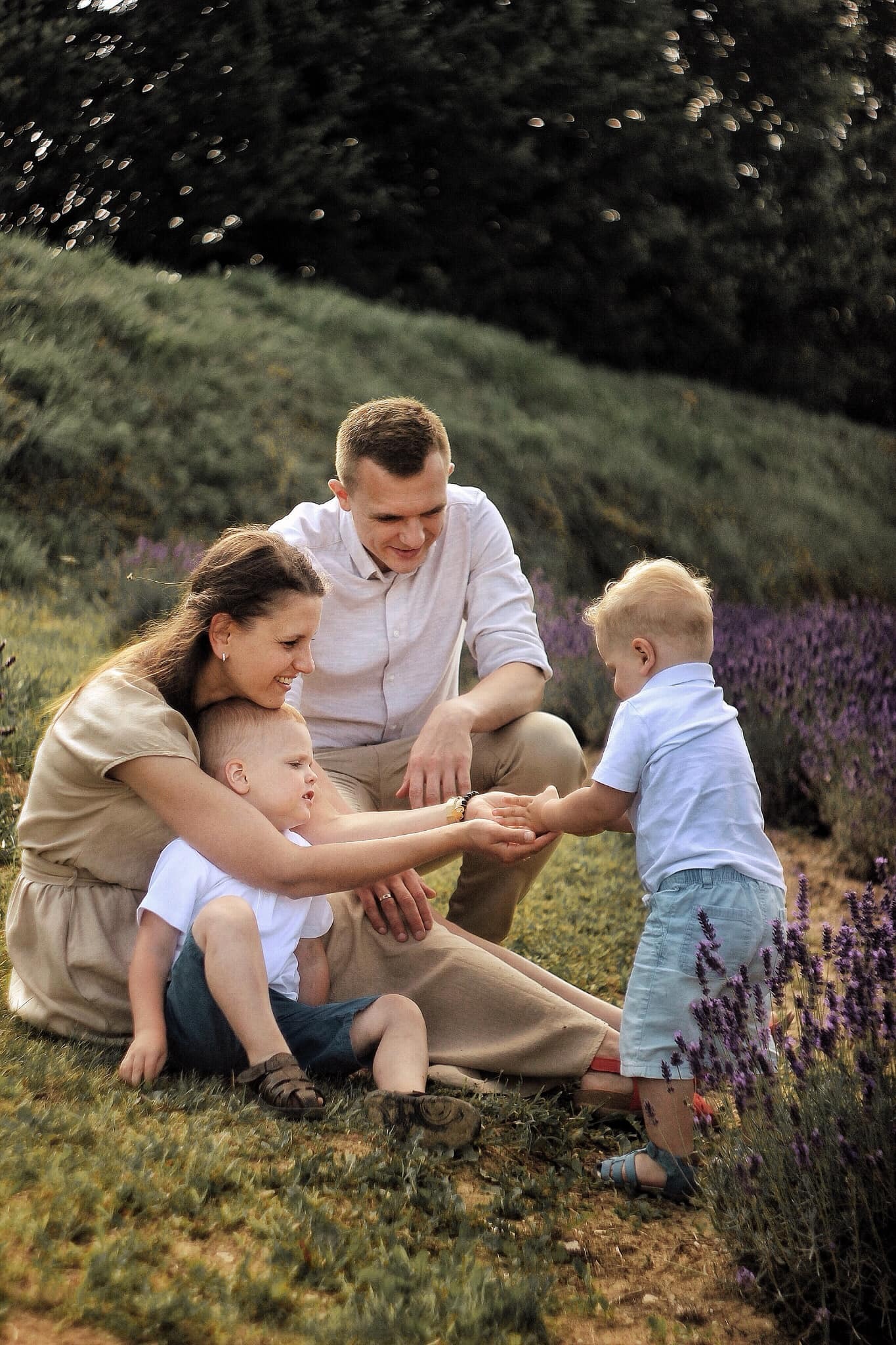 Rodzina z dwójką małych dzieci spędza czas na łące lawendy, jasna odzież, ciepłe światło.