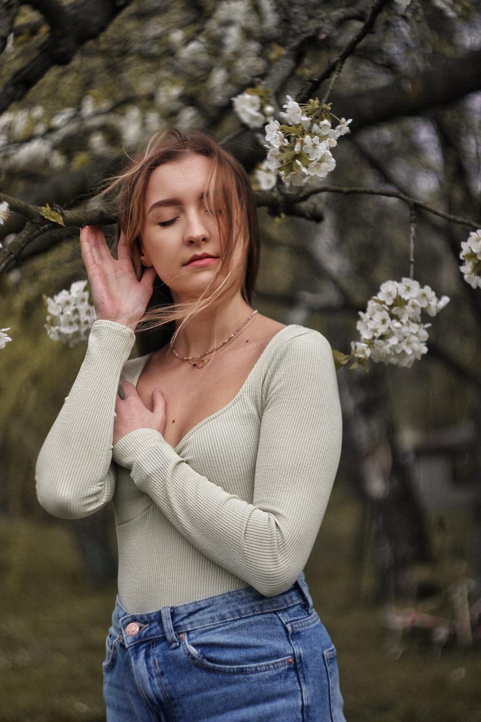 Portret kobiety w Nowym Brzesku, pozującej pod kwitnącym drzewem z delikatnym makijażem i z zamkniętymi oczami.