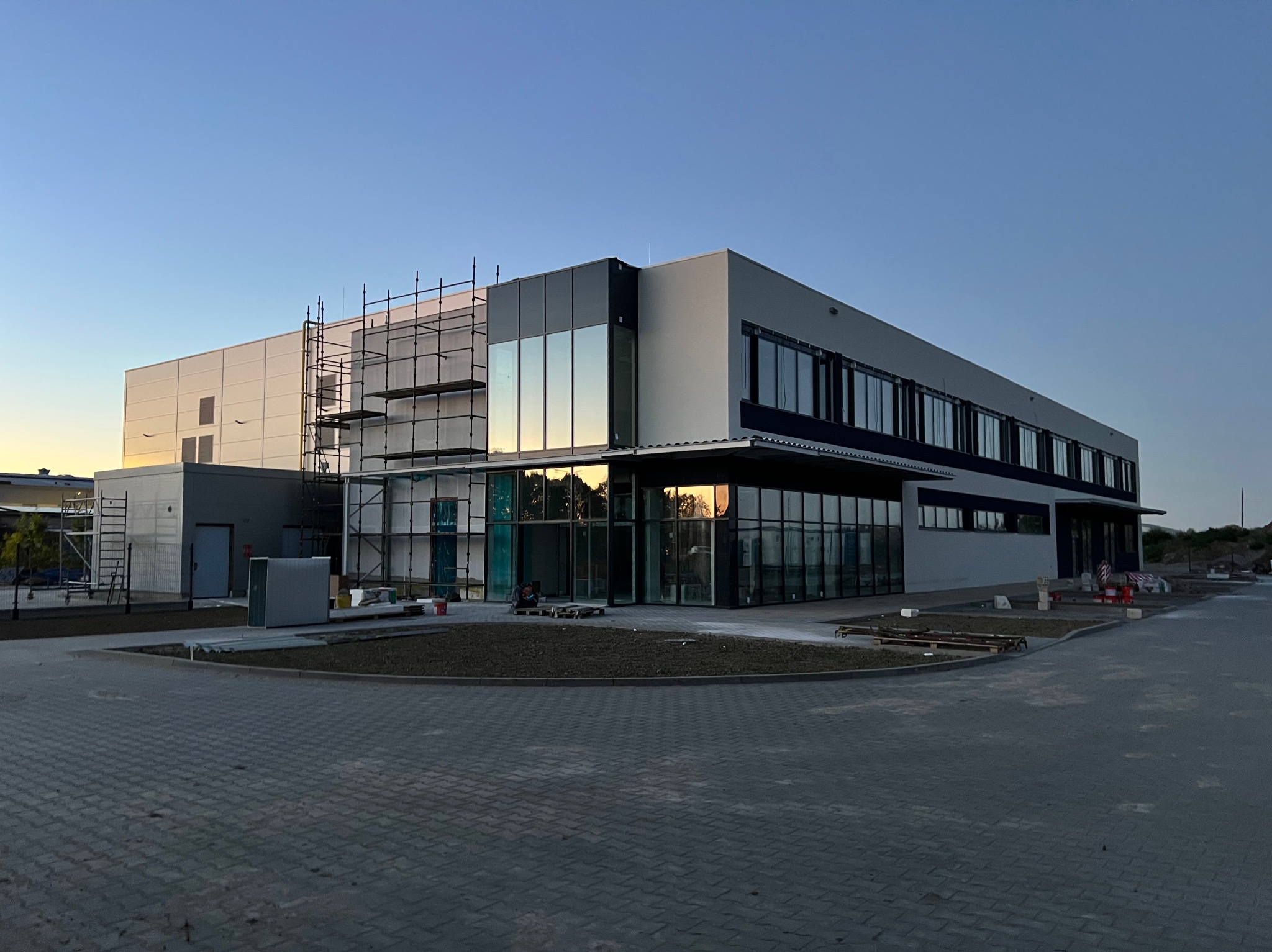 Nowoczesny budynek biurowy z elementami szklanymi w Uskorz Mały, częściowo w rusztowaniach. Widoczne prace wykończeniowe i zagospodarowanie terenu.