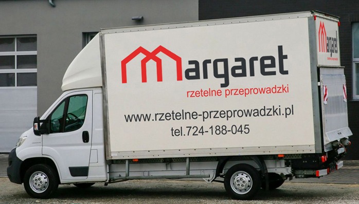 Biały samochód dostawczy z grafiką firmy przeprowadzkowej Margaret, prezentujący logo, adres strony internetowej i numer telefonu na tle szarego budynku.