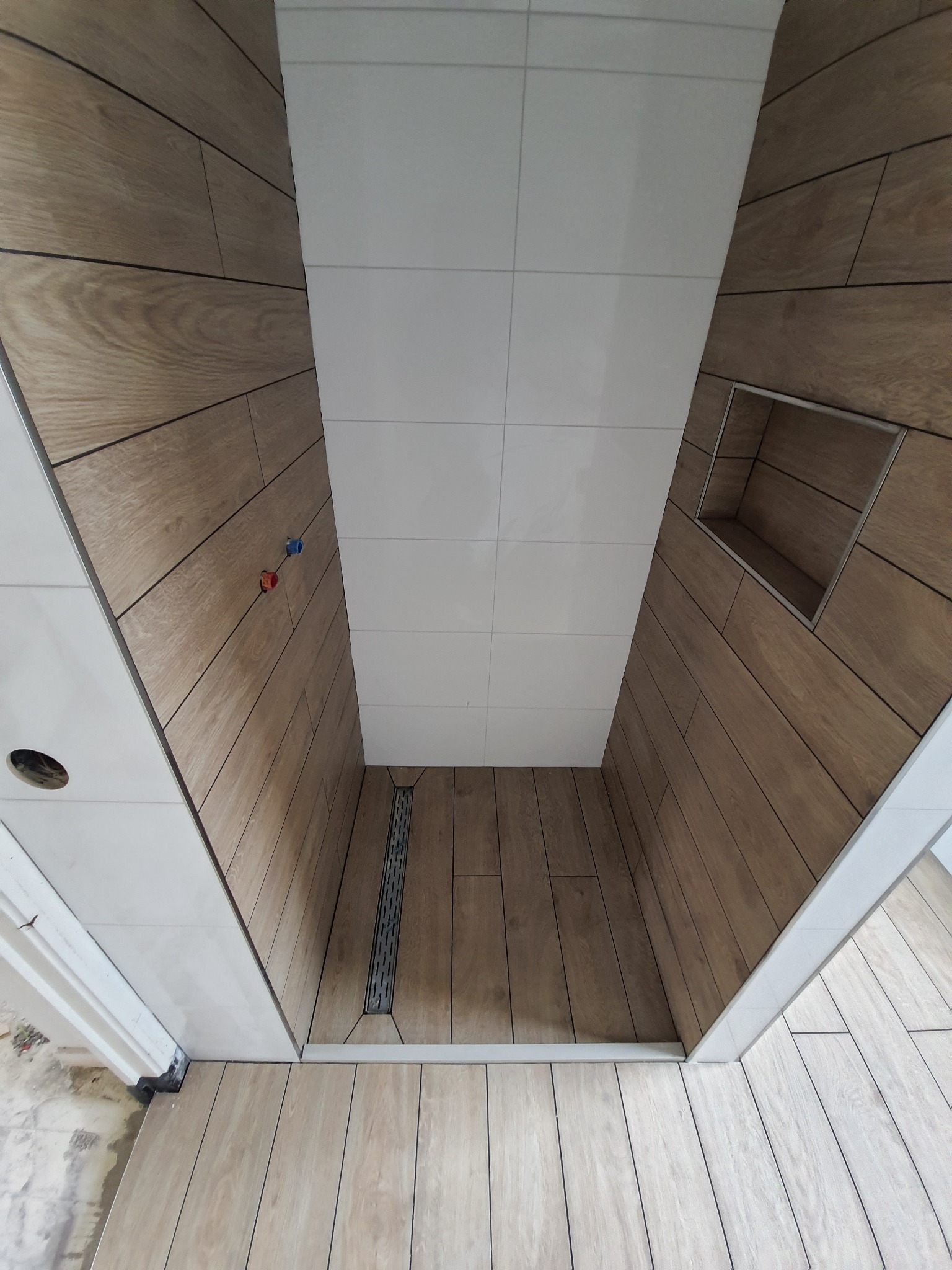 Wnętrze kabiny prysznicowej wyłożonej płytkami imitującymi drewno, z odpływem liniowym i wnęką w ścianie, widok z góry.