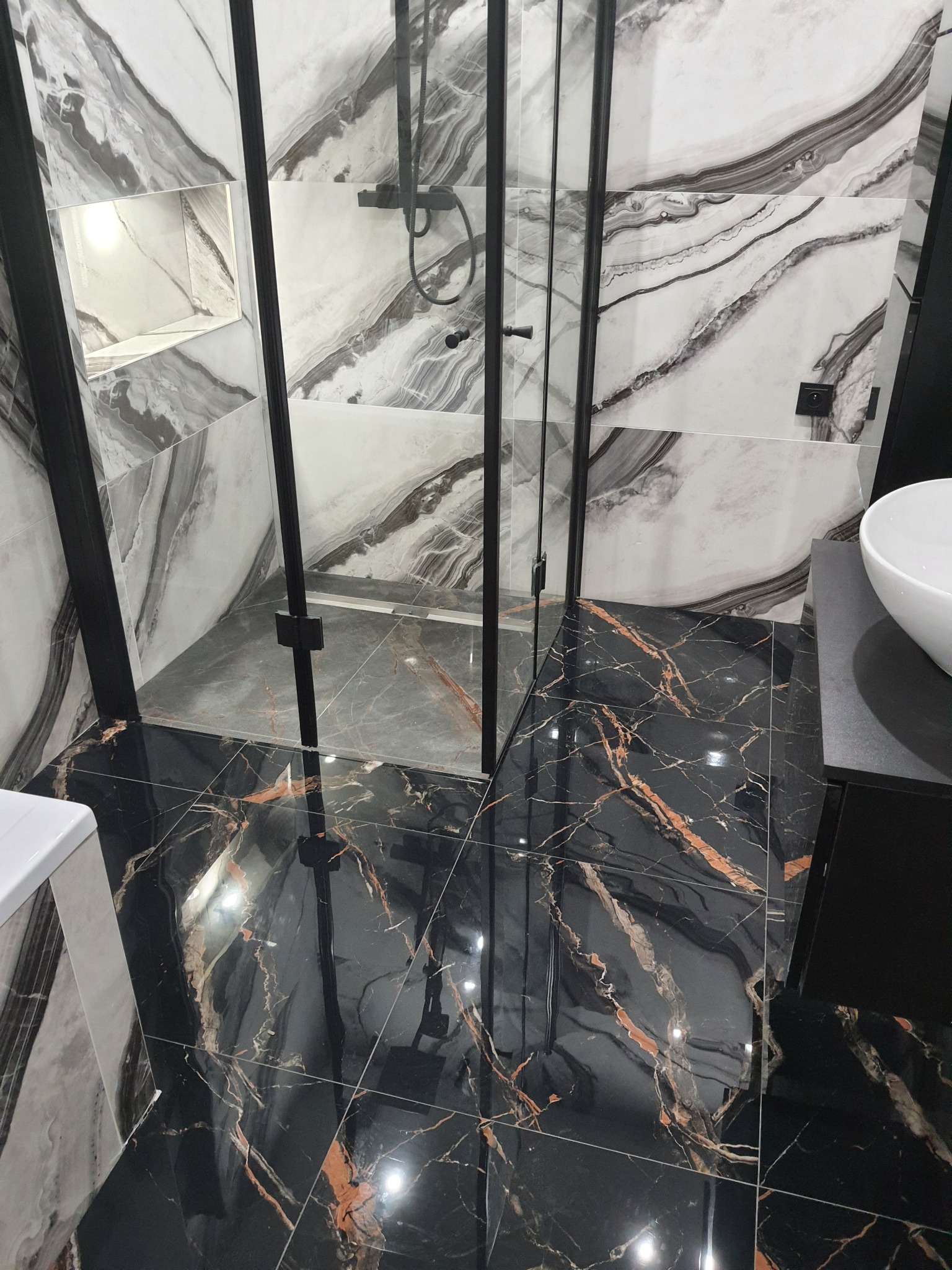 Nowoczesna łazienka z kabiną prysznicową typu walk-in, wykończona płytkami imitującymi marmur w odcieniach bieli i czerni z elementami miedzi, czarna armatura i odpływ liniowy.