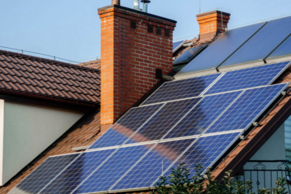 Instalacja fotowoltaiczna na dachu dwuspadowym z ceglanym kominem, widoczna z dołu pod kątem.
