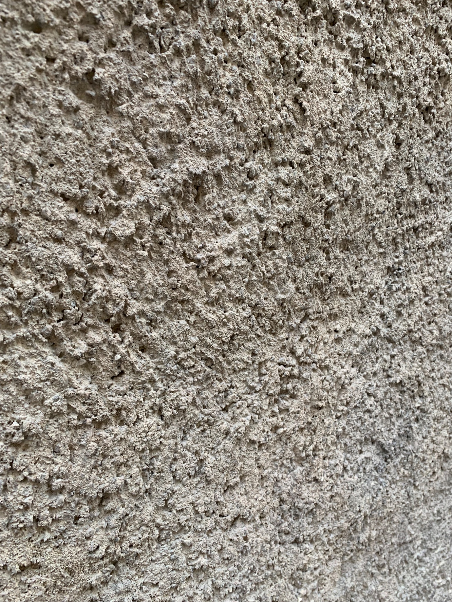 Szorstka, beżowa faktura elewacji zewnętrznej z bliska, ukazująca nierównomierne nałożenie tynku barankowego.