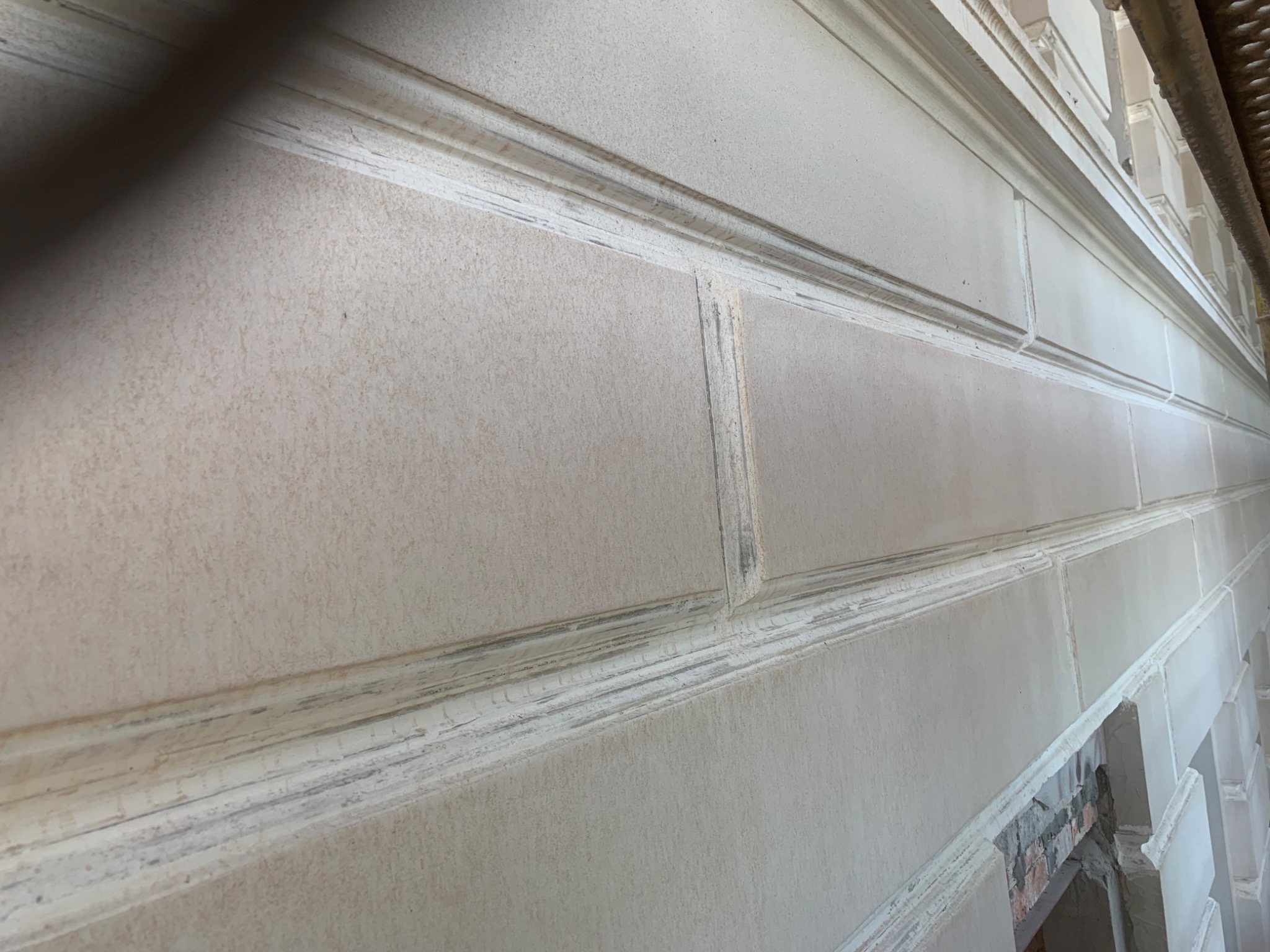 Elewacja budynku z dekoracyjnymi elementami, widoczne ślady niedokładnego wykończenia i pozostałości farby w zagłębieniach.