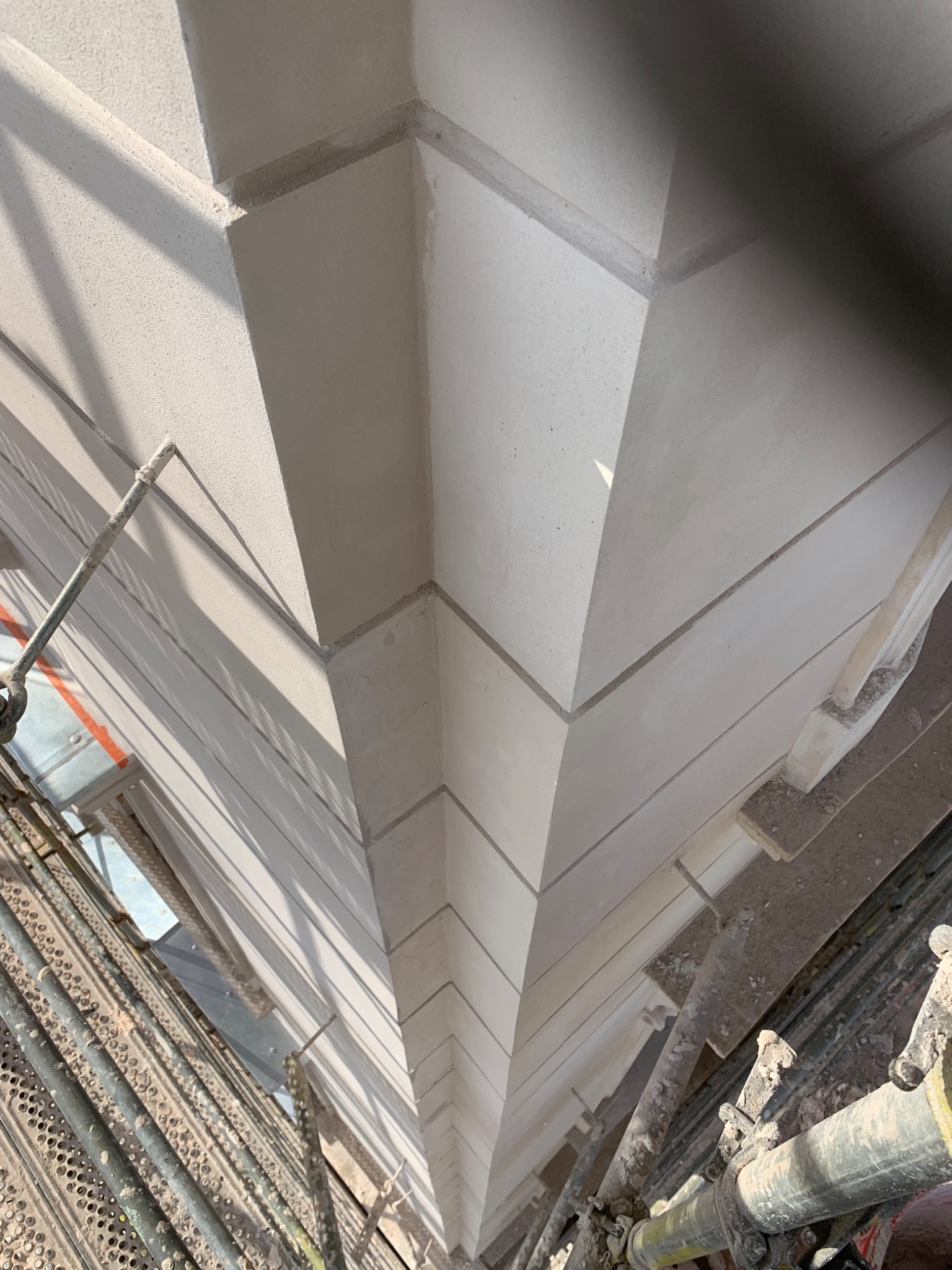 Świeżo otynkowany narożnik elewacji budynku, widoczny ze stojącego obok rusztowania.