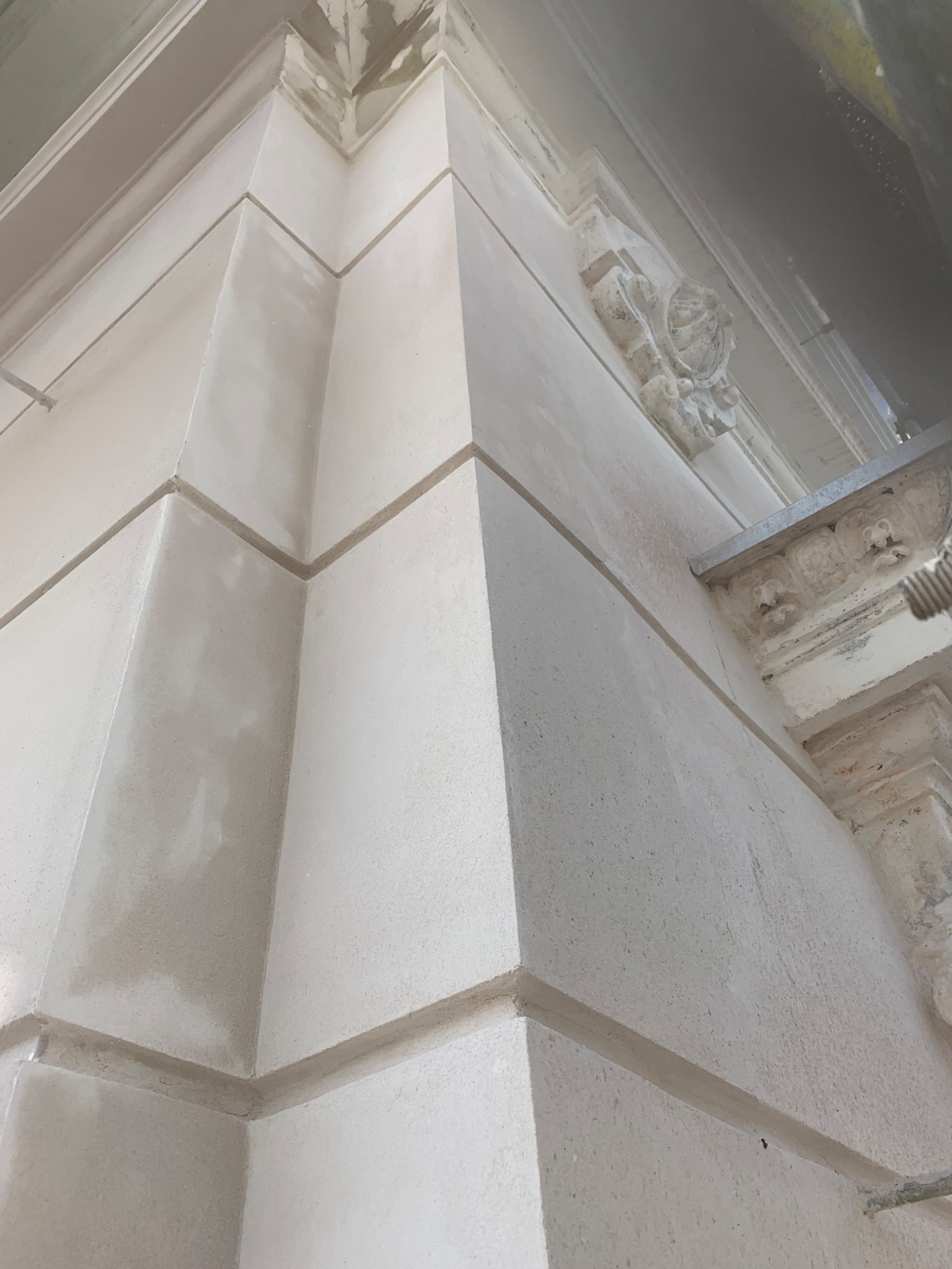 Fragment elewacji budynku z dekoracyjnymi elementami architektonicznymi, w trakcie prac wykończeniowych, widoczne ślady po szpachlowaniu.