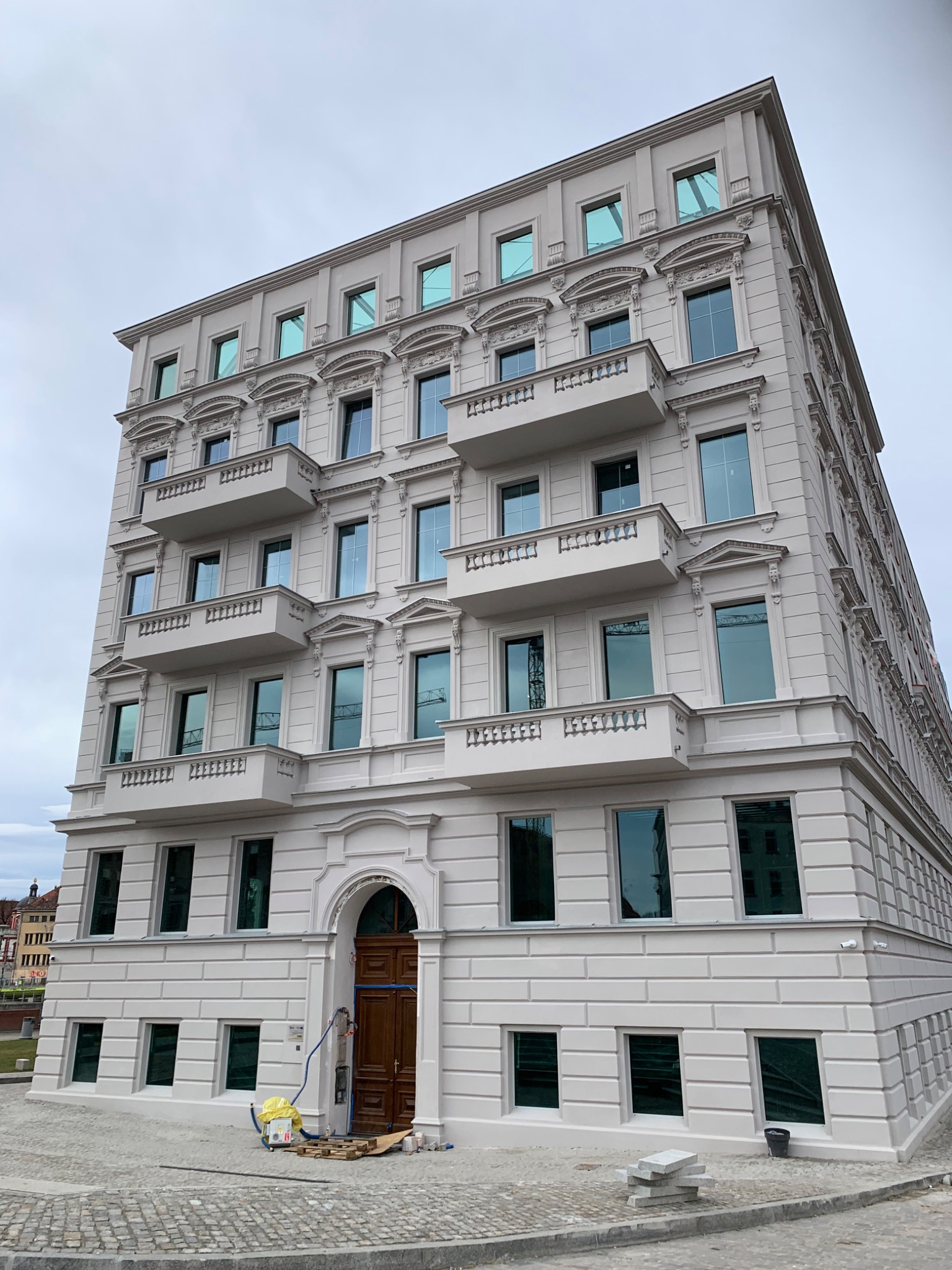 Wielopiętrowy budynek mieszkalny z balkonami w stylu klasycystycznym, świeżo po remoncie, z widocznymi śladami prac wykończeniowych przy wejściu.