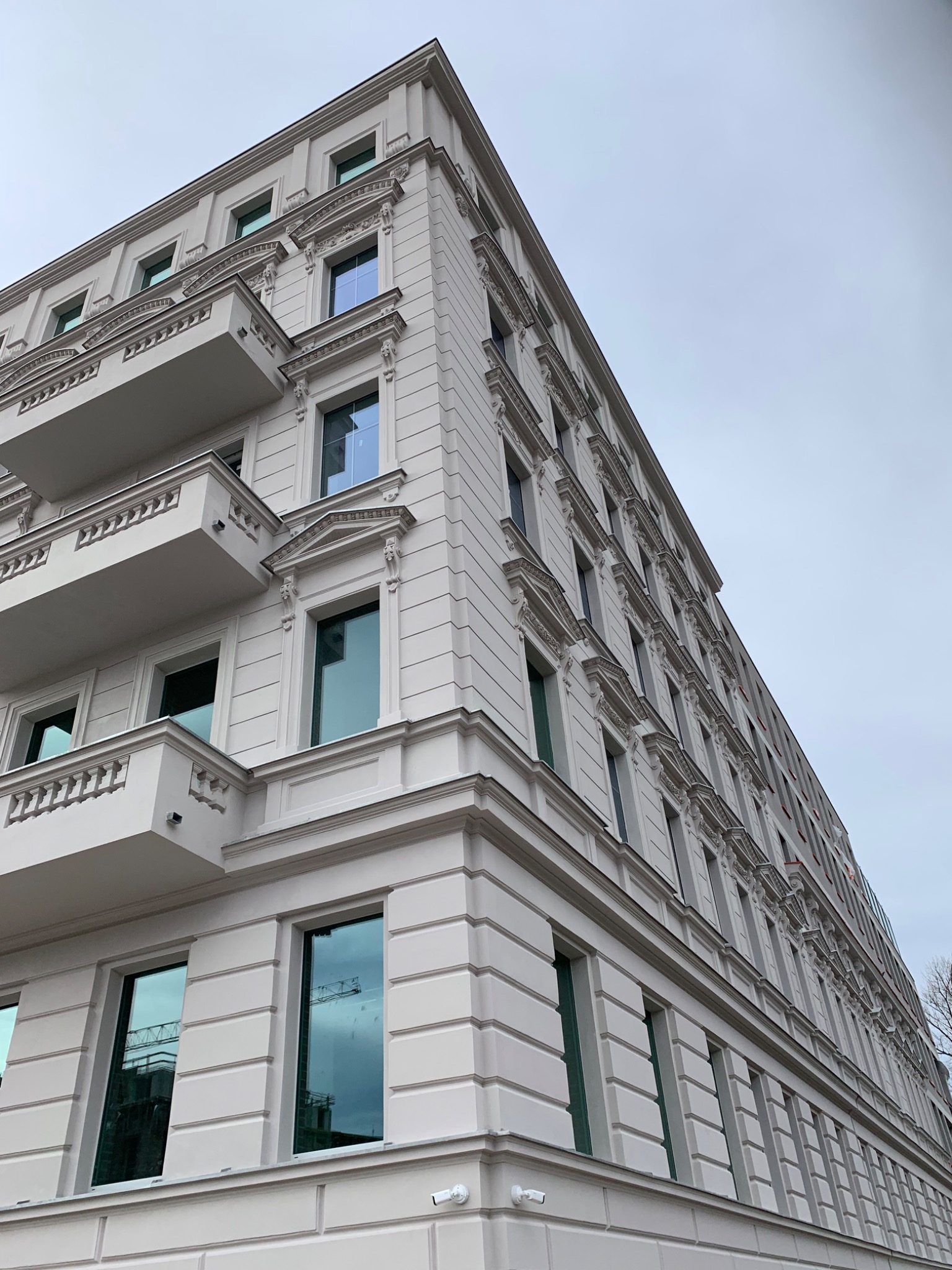 Odnowiona elewacja wielopiętrowego budynku w Świdnicy, z widocznymi balkonami i ozdobnymi detalami architektonicznymi, sfotografowana pod kątem z dołu w pochmurny dzień.