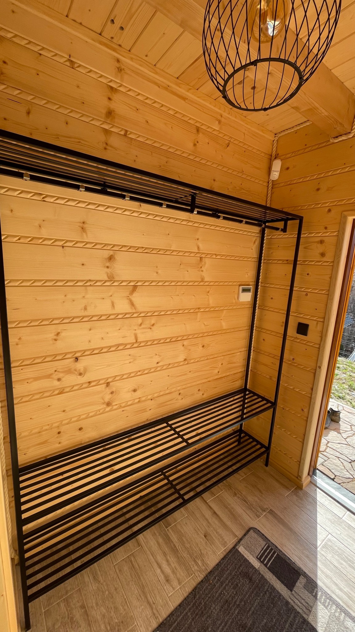 Metalowa konstrukcja garderoby z półkami w drewnianym wnętrzu domku letniskowego, widok z dołu na lampę sufitową.