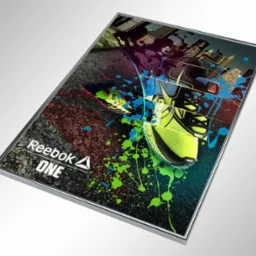 Oprawiona w ramkę grafika reklamowa buta sportowego Reebok ONE z elementami miejskiego krajobrazu i kolorowymi plamami farby, umieszczona na jasnoszarym tle.