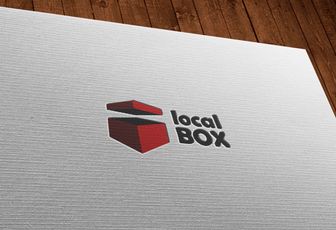 Logo 'local BOX' z otwartym, czerwonym pudełkiem na teksturowanym, białym tle z drewnianym blatem w tle.
