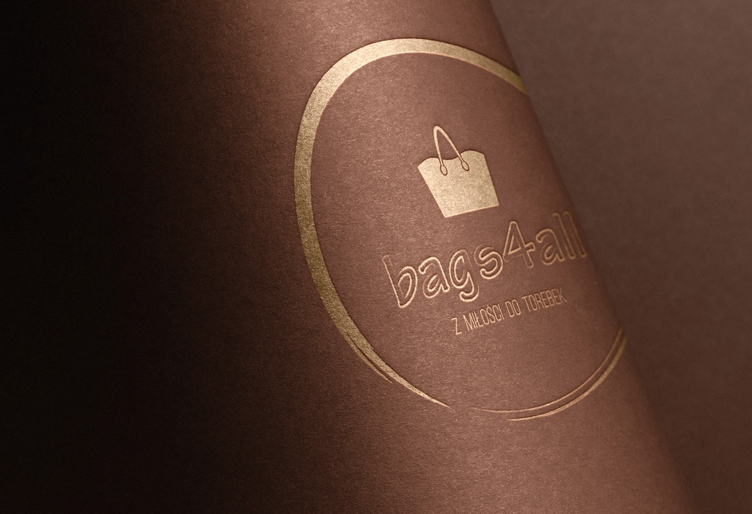 Zbliżenie na brązowy papier z wytłoczonym złotym logo 'bags4all' i hasłem 'z miłości do torebek' w owalnej ramce.