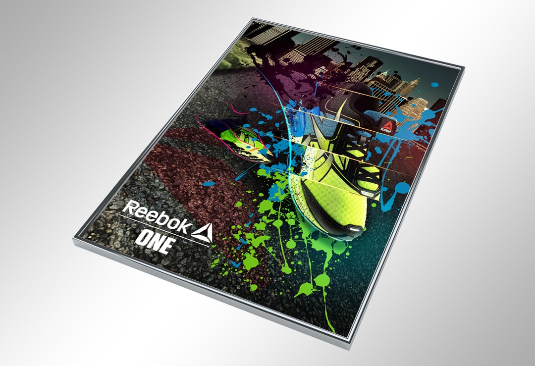 Oprawiona w ramkę grafika reklamowa buta sportowego Reebok ONE z elementami miejskiego krajobrazu i kolorowymi plamami farby, umieszczona na jasnoszarym tle.