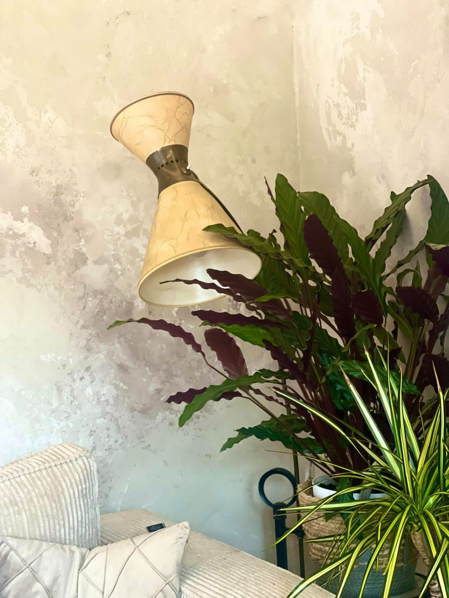 Lampa stołowa z abażurem w stylu retro, obok rośliny doniczkowe na tle ściany z efektem dekoracyjnego tynku. Elementy wystroju wnętrza.