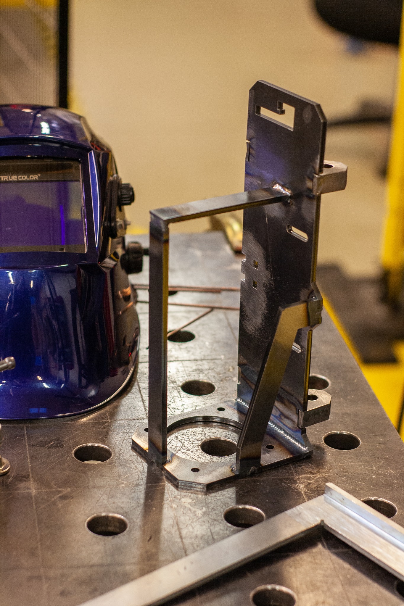 Metalowa konstrukcja spawana na perforowanym stole spawalniczym, obok niebieska maska spawalnicza True Color.