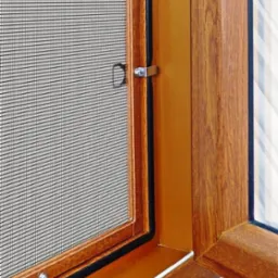 Zamknięte okno z brązową ramą i siatką przeciw owadom, widoczne metalowe zatrzaski.