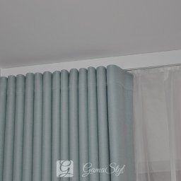 Dekoracje okien | Karnisze, Rolety, Żaluzje | GAMA STYL - Jasnoniebieska, gęsto marszczona zasłona z podszewką, zawieszona na karniszu, obok firanka z woalu, w jasnym wnętrzu.