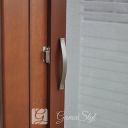 Dekoracje okien | Karnisze, Rolety, Żaluzje | GAMA STYL - Brązowa rama okienna z zamontowaną plisą w kolorze białym, widoczny uchwyt i zamek okna.