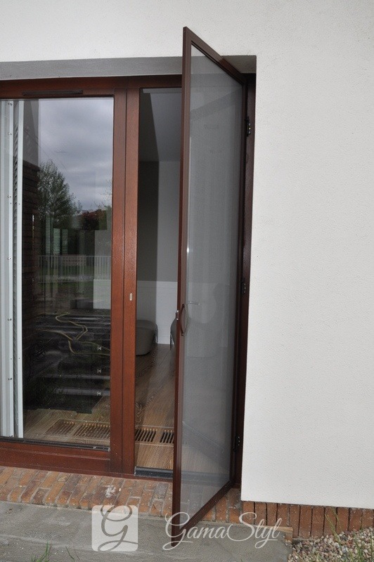 Otwarty brązowy panel moskitierowy na drzwiach balkonowych, widok z zewnątrz