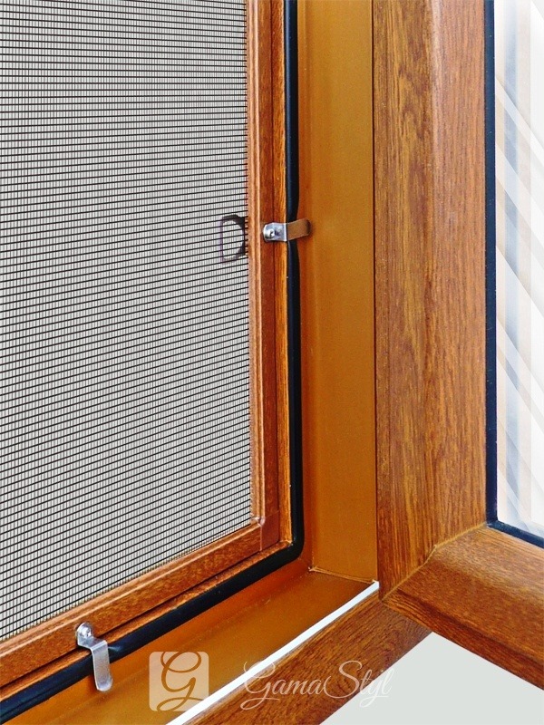 Zamknięte okno z brązową ramą i siatką przeciw owadom, widoczne metalowe zatrzaski.