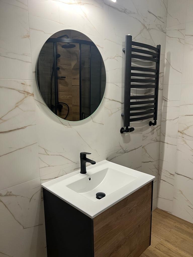 Nowoczesna łazienka z umywalką nablatową, czarną armaturą i grzejnikiem drabinkowym na tle marmurowych płytek.