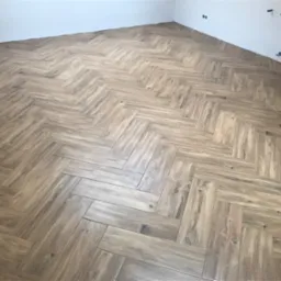 Ułożona podłoga z płytek imitujących drewno w jodełkę francuską, widoczne niedokończone prace wykończeniowe przy ścianie.