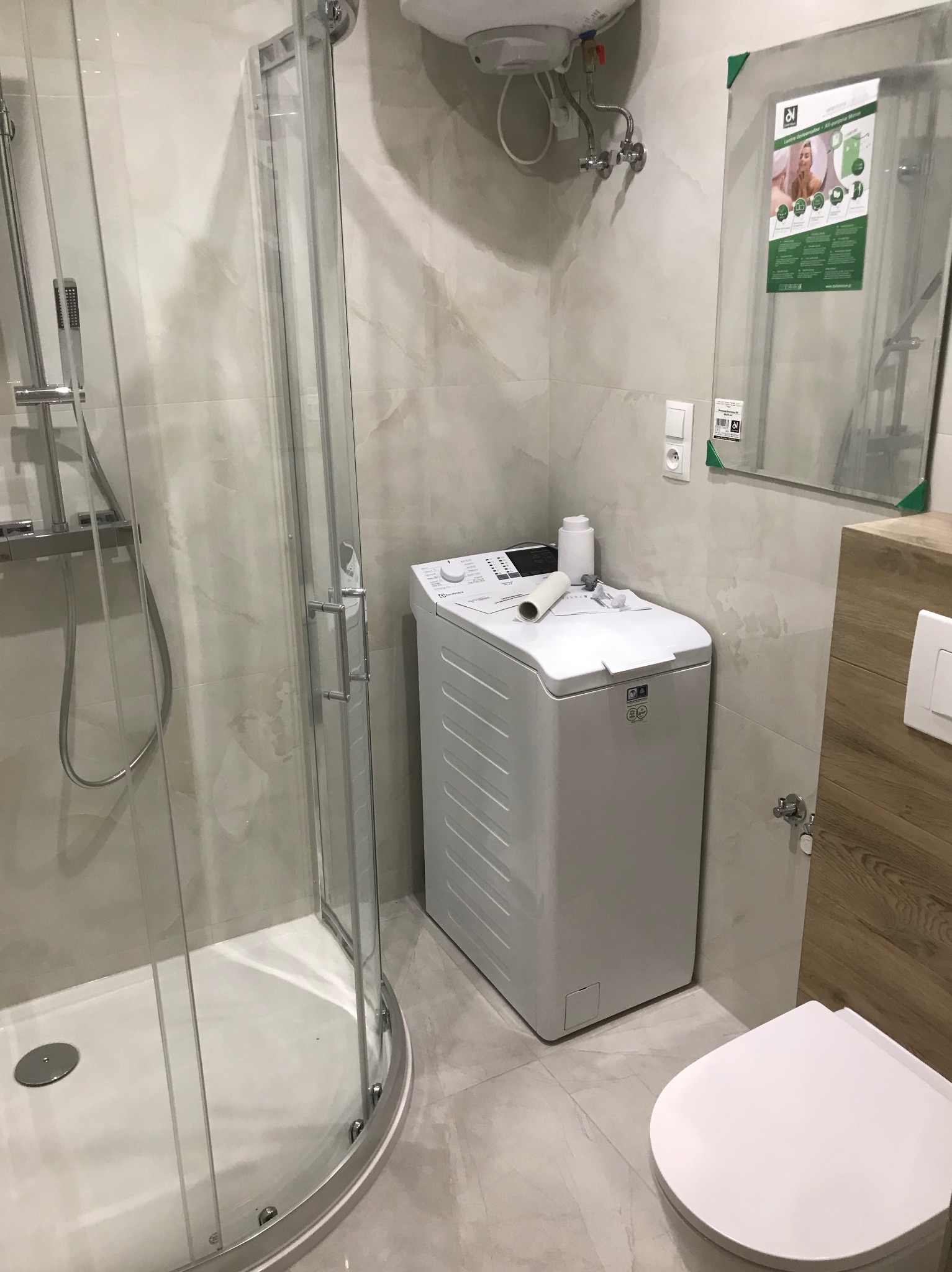 Nowoczesna łazienka z kabiną prysznicową, pralką ładowaną od góry i podwieszaną toaletą, wykończona płytkami imitującymi marmur.