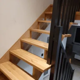 Nowoczesne schody z jasnego drewna z czarną, minimalistyczną balustradą, widok z dołu, oświetlenie naturalne.