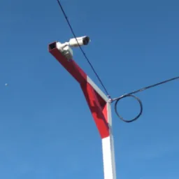 Kamera monitoringu na czerwono-białym słupie z pętlą kabla na tle błękitnego nieba.