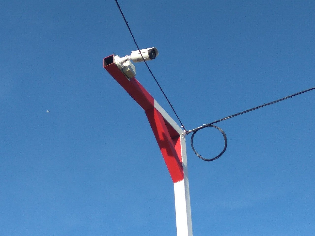 Kamera monitoringu na czerwono-białym słupie z pętlą kabla na tle błękitnego nieba.