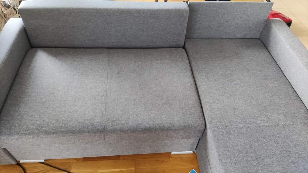 Szary narożnik z tkaniny o wyraźnej fakturze, widoczny z góry, z fragmentem podłogi w tle.