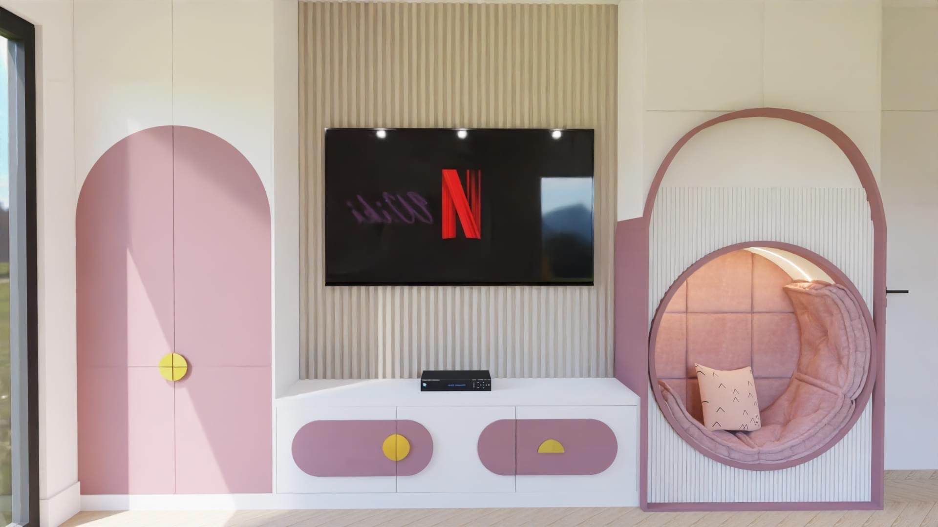 Pokój dziecięcy z zabudową w pastelowych kolorach: różowe drzwi szafy z okrągłym, żółtym uchwytem, niski biały regał pod telewizorem z dekoracyjnymi wstawkami w kształcie okręgów i półokręgów,...
