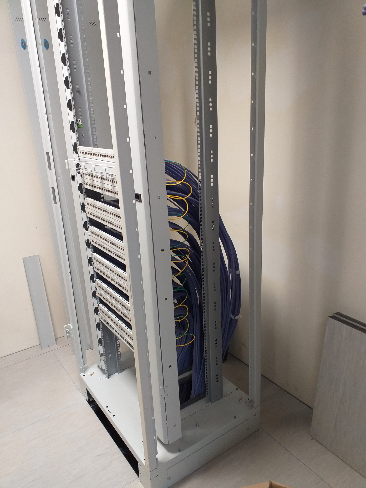 Szare metalowe ramy szafy serwerowej z panelami krosowniczymi i uporządkowanymi kablami w kolorze niebieskim i żółtym.