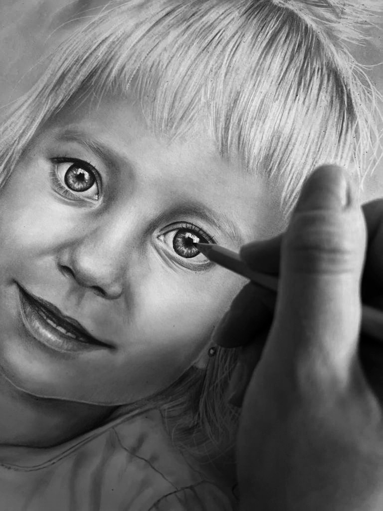 Czarno-biały portret dziewczynki rysowany ołówkiem, z dłonią artysty w kadrze, skupiającego się na detalu oka.