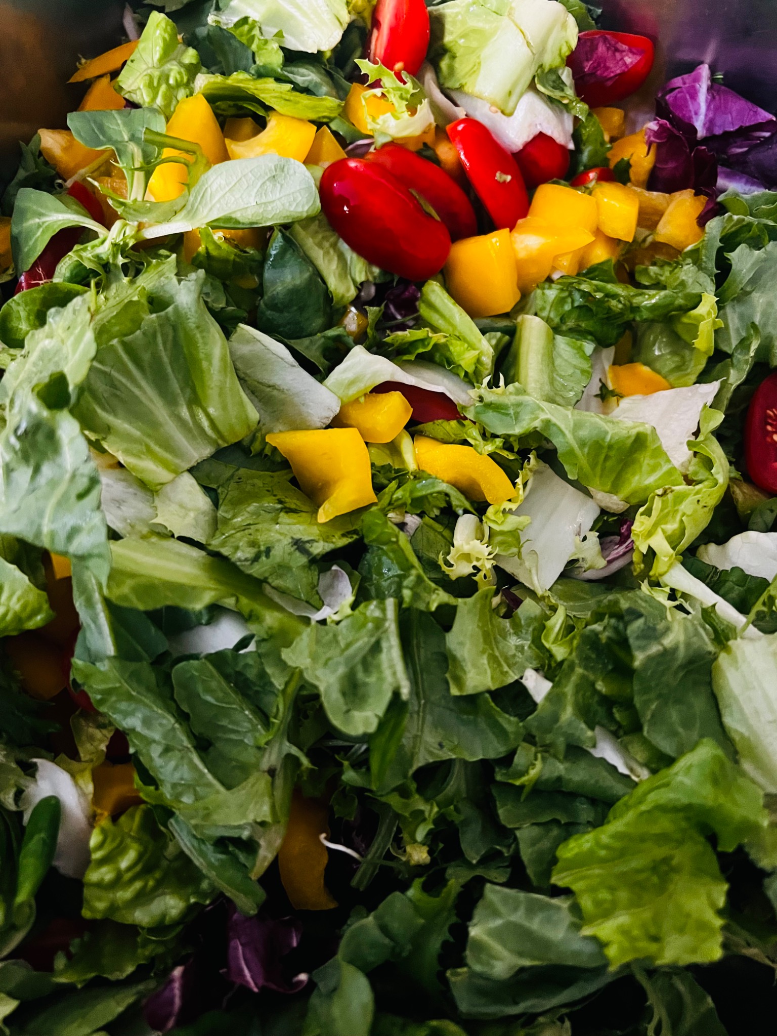 Świeża sałatka z mieszanych sałat, czerwonej i żółtej papryki, pomidorków koktajlowych i fioletowej kapusty, ułożona w metalowej misce.
