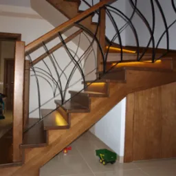 Drewniane schody z oświetleniem LED pod stopniami i ozdobną, metalową balustradą. Na podłodze leżą dziecięce zabawki.