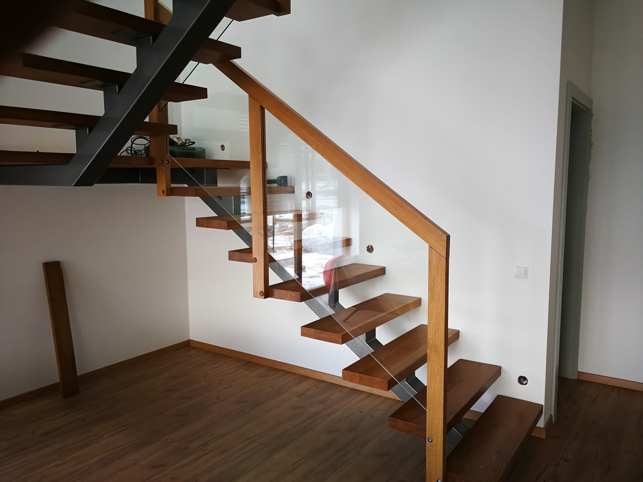 Nowoczesne schody drewniane z metalowymi wspornikami i szklaną balustradą, widok z dołu, parkiet na podłodze, minimalistyczny design.