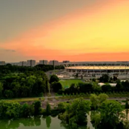 Panorama Ruda Śląska o zmierzchu: stadion miejski otoczony zielenią parkową i budynkami mieszkalnymi, sfotografowany z lotu ptaka przy zachodzącym słońcu.